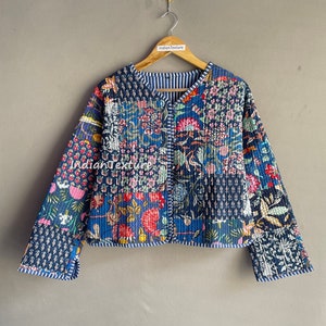 May include: A blue quilted jacket with a floral print. The jacket has a V-neck and a button closure. The sleeves are long and have a striped trim.