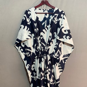 May include: A white and navy blue kaftan with a tie at the waist. The kaftan has a large, abstract print.