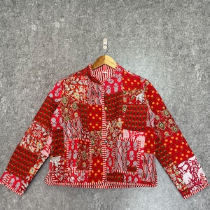 May include: A red quilted jacket with a patchwork design featuring various floral and geometric patterns. The jacket has a mandarin collar and long sleeves.