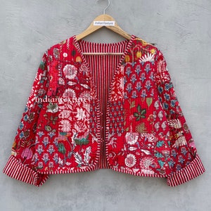 Puede incluir: Una chaqueta acolchada roja con estampado floral y rayas blancas en las mangas. La chaqueta tiene cuello en V y está abierta por delante. El texto "Indian Texture" es visible en la percha.
