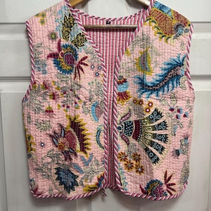 May include: A pink quilted vest with a floral print and a striped lining. The vest has a V-neck and a tie closure.
