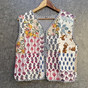 May include: A white quilted waistcoat with a patchwork design featuring floral and animal prints. The waistcoat has a V-neck and a tie closure.