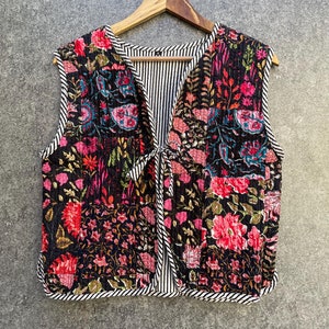 May include: A black quilted vest with a floral print and a striped lining. The vest has a tie closure at the neck.