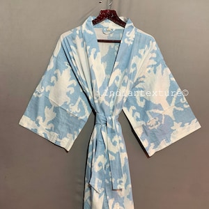K&ouml;nnte beinhalten: Eine hellblaue Baumwollrobe mit wei&szlig;em Blumenmuster. Die Robe hat einen Bindeg&uuml;rtel und lange &Auml;rmel. Der Text "Indiantexture&copy;" ist auf die Robe gedruckt.