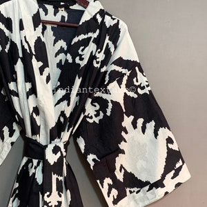 May include: Black and white patterned robe with a long sleeve and a sash tie. The robe has a V-neck and is made of a soft, lightweight fabric.