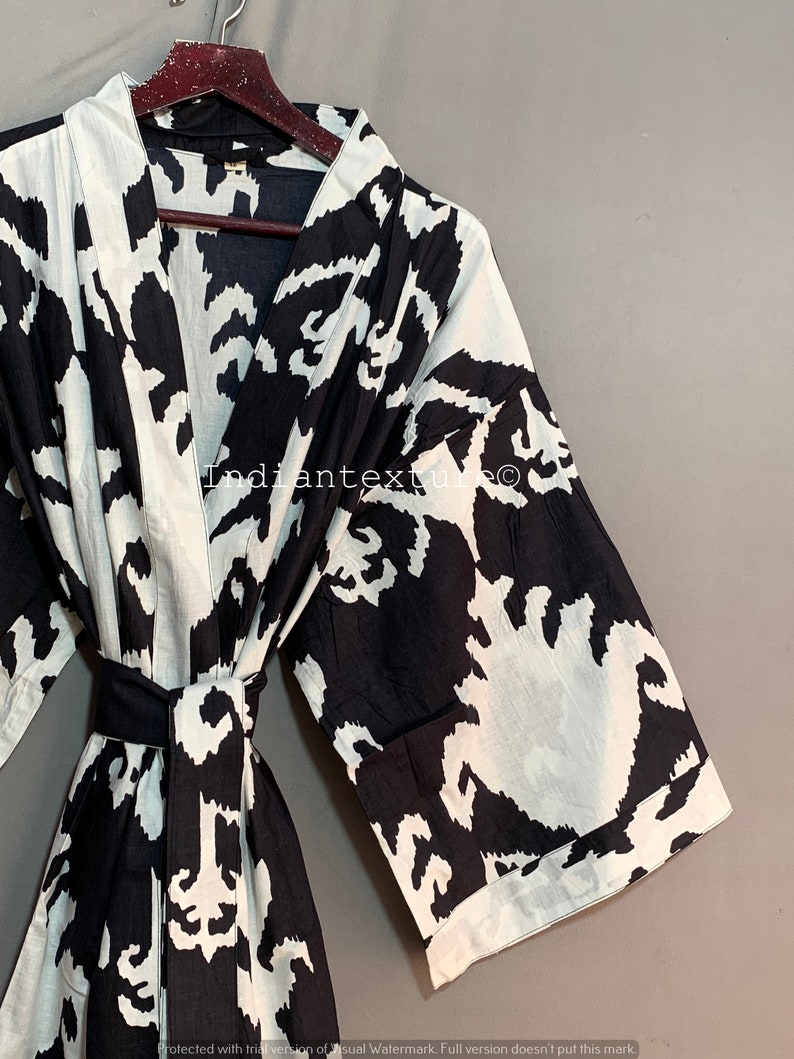 May include: Black and white patterned robe with a long sleeve and a sash tie. The robe has a V-neck and is made of a soft, lightweight fabric.