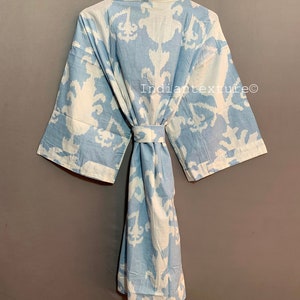 K&ouml;nnte beinhalten: Eine hellblaue Baumwollrobe mit einem wei&szlig;en Ikat-Muster. Die Robe hat einen Bindeg&uuml;rtel und lange &Auml;rmel. Der Text "Indiantexture&reg;" ist auf die Robe gedruckt.