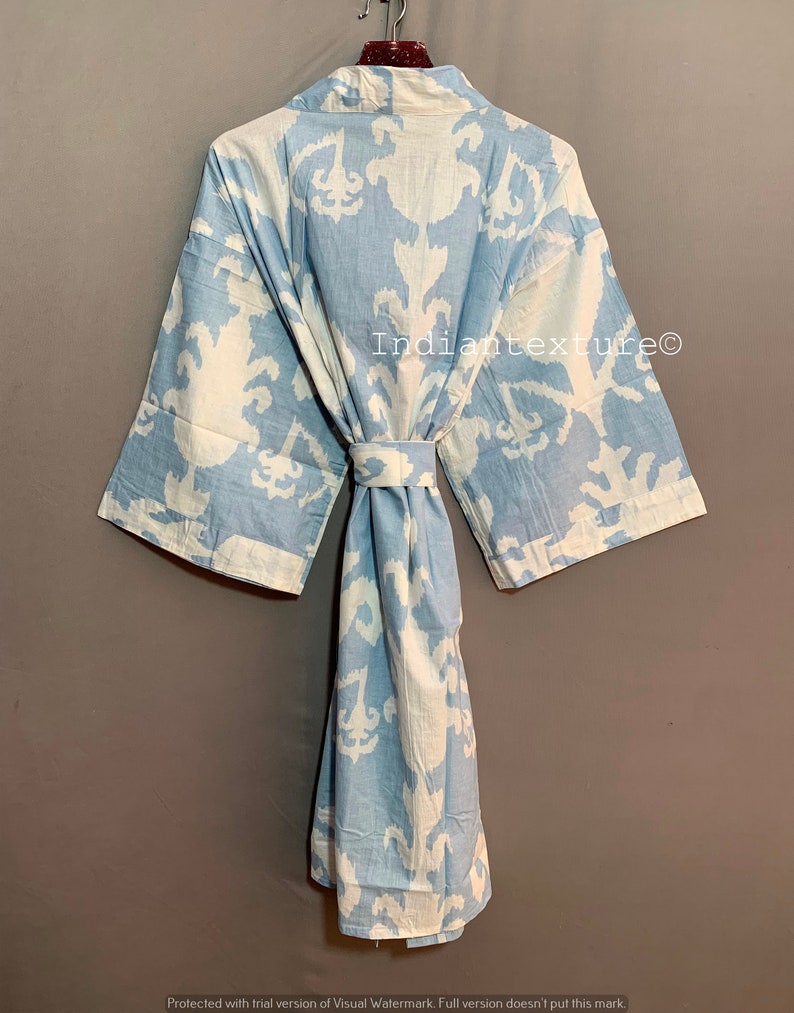 K&ouml;nnte beinhalten: Eine hellblaue Baumwollrobe mit einem wei&szlig;en Ikat-Muster. Die Robe hat einen Bindeg&uuml;rtel und lange &Auml;rmel. Der Text "Indiantexture&reg;" ist auf die Robe gedruckt.