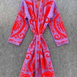 Puede incluir: Una bata morada con un estampado floral rojo. La bata tiene un cintur&oacute;n de atar y un forro a rayas rojo y blanco.