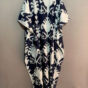 May include: A long, flowing white and navy blue kaftan with a geometric pattern. The kaftan has a wide, round neckline and short sleeves.