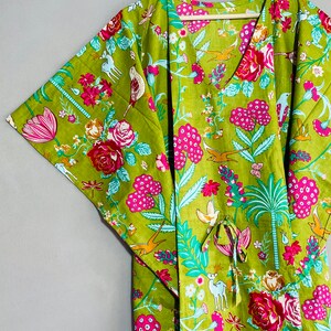Peut inclure: Une kaftan verte &agrave; imprim&eacute; floral avec des fleurs roses, des feuilles vertes et des oiseaux. La kaftan a un col en V et une ceinture &agrave; la taille. Le texte "INDIAN TEXTURE" est &eacute;crit sur le cintre.