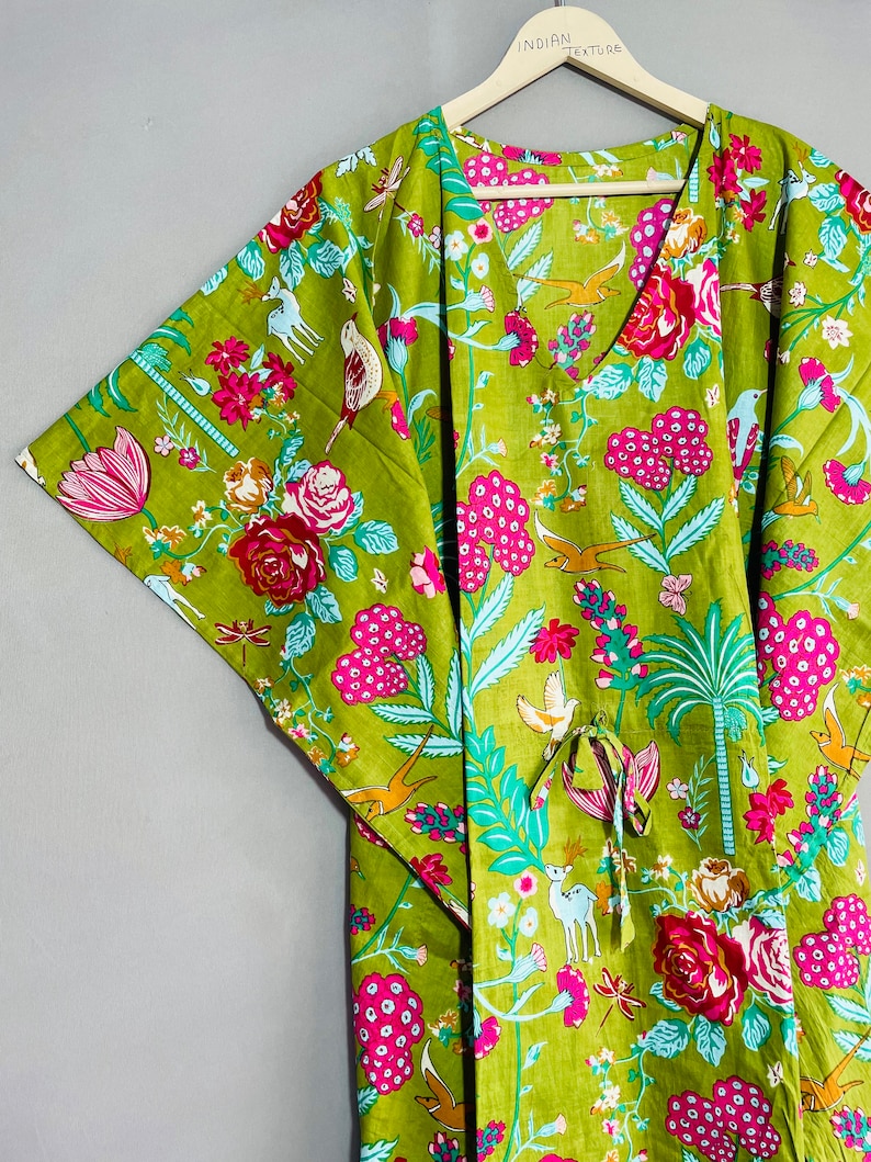 Peut inclure: Une kaftan verte &agrave; imprim&eacute; floral avec des fleurs roses, des feuilles vertes et des oiseaux. La kaftan a un col en V et une ceinture &agrave; la taille. Le texte "INDIAN TEXTURE" est &eacute;crit sur le cintre.