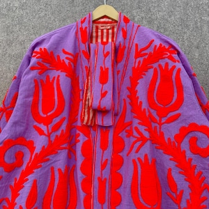 Puede incluir: Una chaqueta bordada de color morado y rojo con un patr&oacute;n floral. La chaqueta tiene una silueta larga y fluida y es perfecta para superponer.