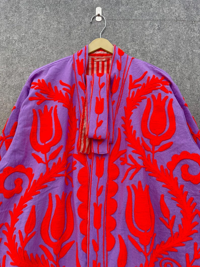 Puede incluir: Una chaqueta bordada de color morado y rojo con un patr&oacute;n floral. La chaqueta tiene una silueta larga y fluida y es perfecta para superponer.