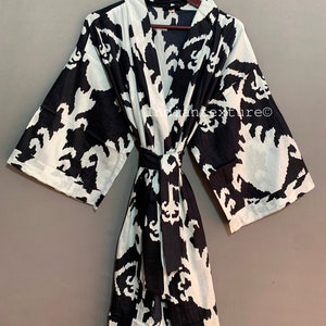May include: A black and white patterned kimono robe with a tie belt. The pattern is a stylized floral design. The robe is hanging on a wooden hanger.
