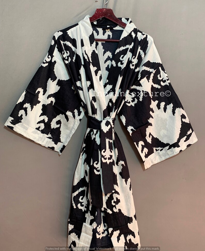May include: A black and white patterned kimono robe with a tie belt. The pattern is a stylized floral design. The robe is hanging on a wooden hanger.