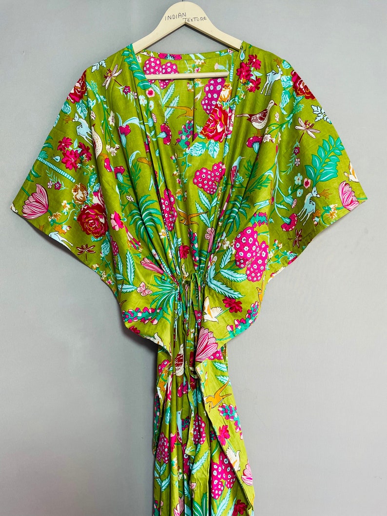 Peut inclure: Une kaftan verte &agrave; imprim&eacute; floral avec des fleurs roses, bleues et blanches, des oiseaux et d'autres motifs. La kaftan a un col en V et des manches courtes. Elle est nou&eacute;e &agrave; la taille avec un cordon.