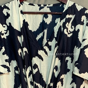 May include: A black and white abstract print kaftan with a V-neckline and short sleeves. The kaftan is hanging on a wooden hanger. The text "Indiantexture&copy;" is visible on the fabric.