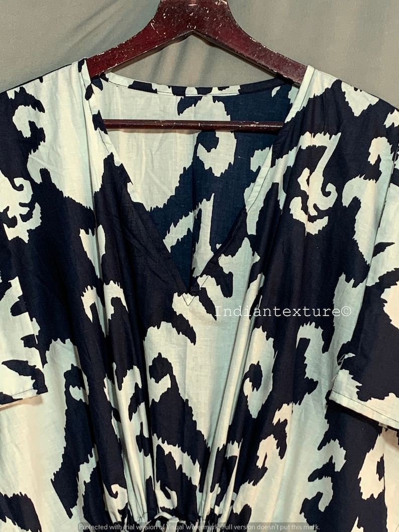 May include: A black and white abstract print kaftan with a V-neckline and short sleeves. The kaftan is hanging on a wooden hanger. The text "Indiantexture&copy;" is visible on the fabric.