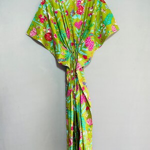 Peut inclure: Une kaftan verte &agrave; imprim&eacute; floral avec des fleurs et des oiseaux roses, bleus et blancs. La kaftan a un col en V et des manches courtes.