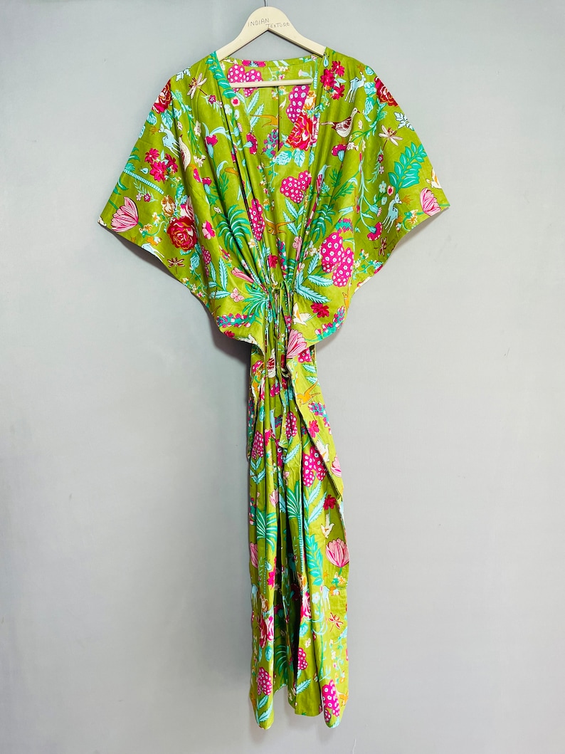 Peut inclure: Une kaftan verte &agrave; imprim&eacute; floral avec des fleurs et des oiseaux roses, bleus et blancs. La kaftan a un col en V et des manches courtes.