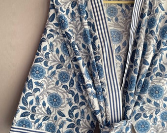 Könnte beinhalten: Ein weißer und blauer floral bedruckter Bademantel mit blau-weißem Streifenbesatz. Der Bademantel hat einen Bindegürtel und eine Tasche auf der linken Seite. Der Text "INDIAN TEXTURE" ist auf dem Holzbügel geschrieben.
