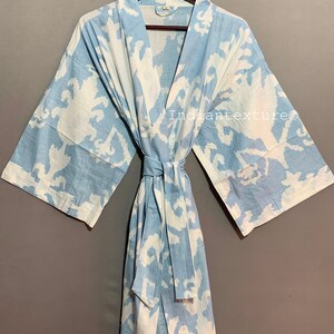 K&ouml;nnte beinhalten: Eine hellblaue Baumwollrobe mit einem wei&szlig;en abstrakten Muster. Die Robe hat einen Bindeg&uuml;rtel und lange &Auml;rmel.
