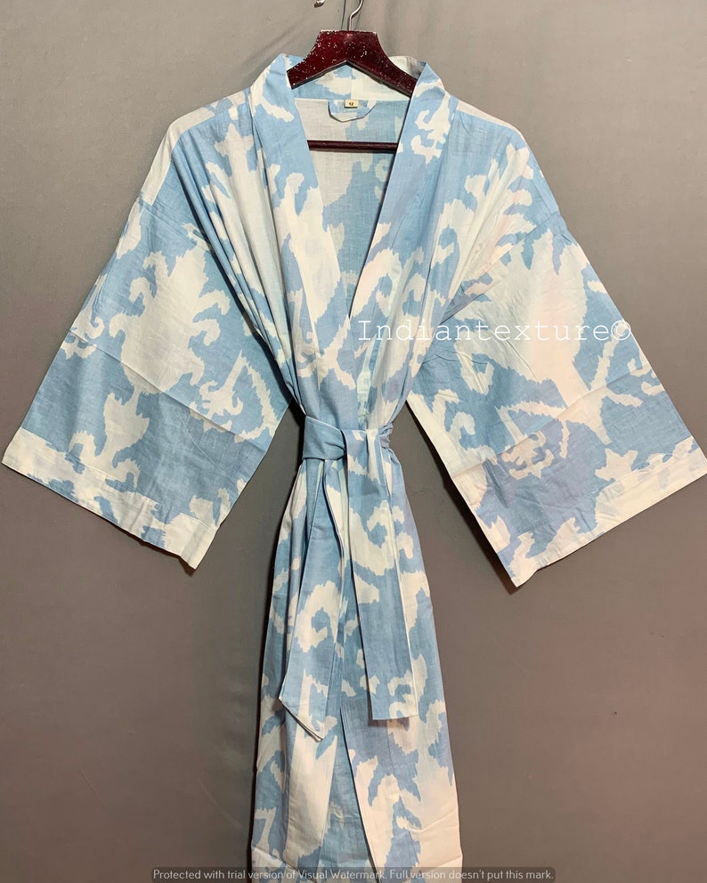 K&ouml;nnte beinhalten: Eine hellblaue Baumwollrobe mit einem wei&szlig;en abstrakten Muster. Die Robe hat einen Bindeg&uuml;rtel und lange &Auml;rmel.