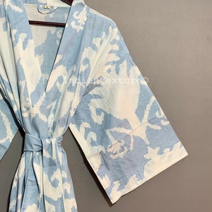 K&ouml;nnte beinhalten: Eine hellblaue Baumwollrobe mit einem wei&szlig;en abstrakten Muster. Die Robe hat einen Bindeg&uuml;rtel und lange &Auml;rmel.
