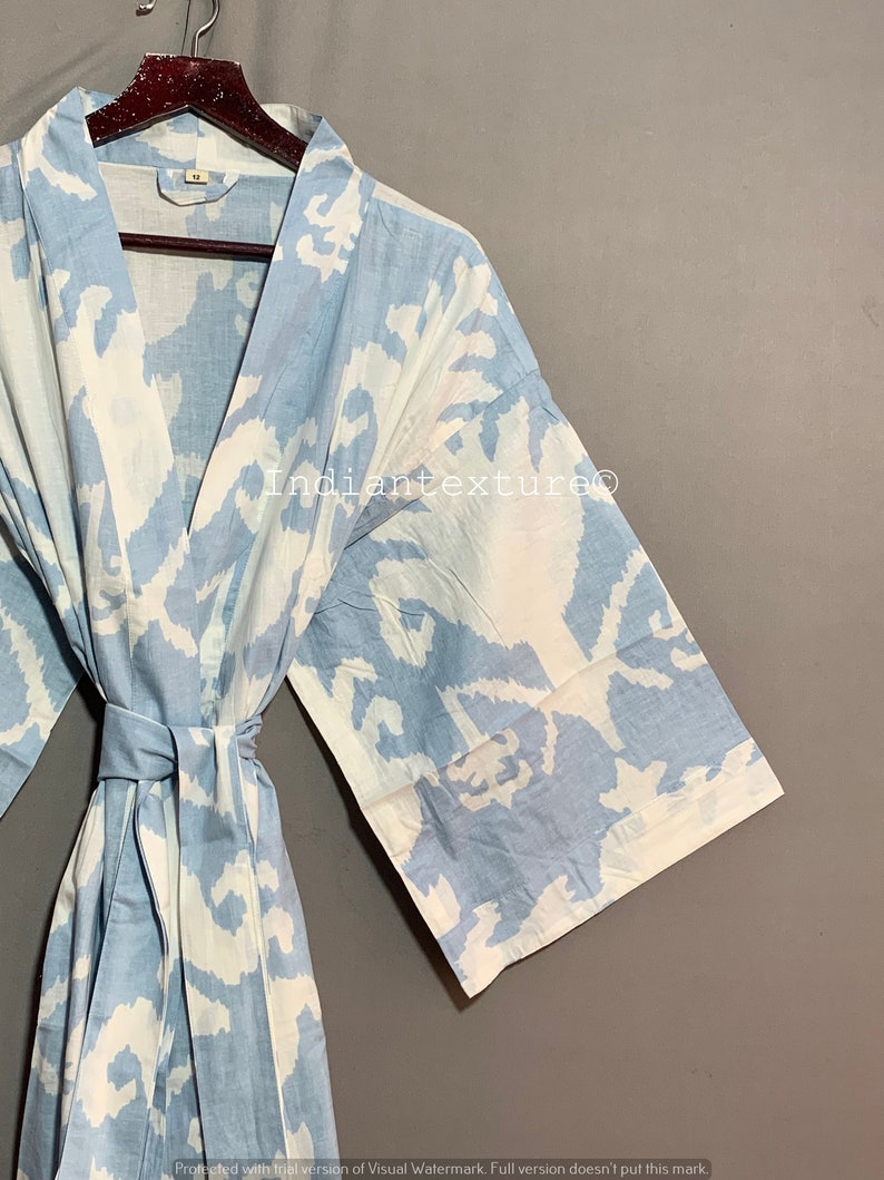 K&ouml;nnte beinhalten: Eine hellblaue Baumwollrobe mit einem wei&szlig;en abstrakten Muster. Die Robe hat einen Bindeg&uuml;rtel und lange &Auml;rmel.