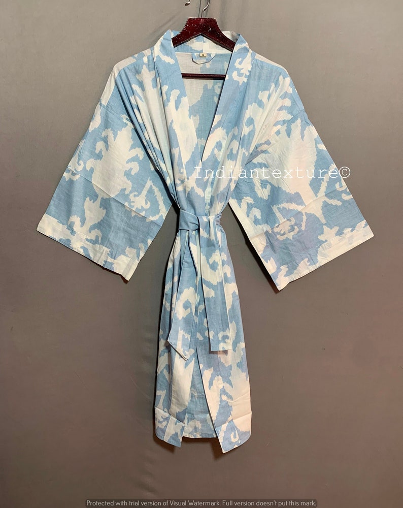 K&ouml;nnte beinhalten: Eine hellblaue Baumwollrobe mit wei&szlig;em Blumenmuster. Die Robe hat einen Bindeg&uuml;rtel und lange &Auml;rmel. Der Text "Indiantexture&copy;" ist auf die Robe gedruckt.