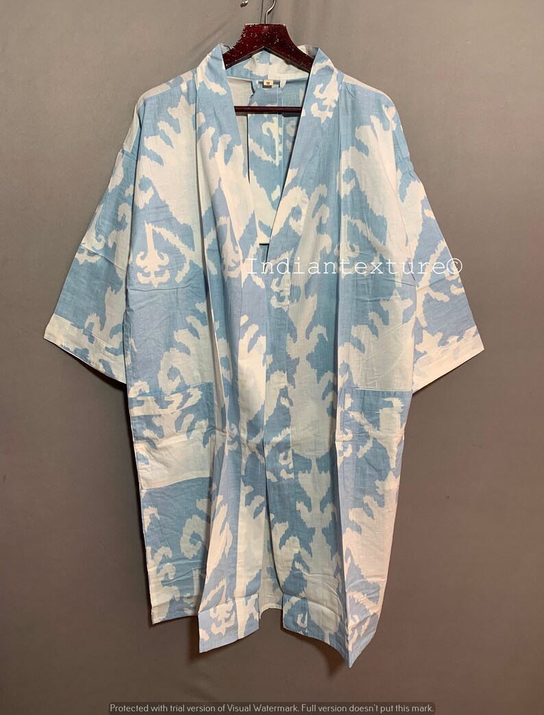 K&ouml;nnte beinhalten: Ein hellblauer Kimono mit einem wei&szlig;en und hellblauen Ikat-Muster. Der Kimono hat einen V-Ausschnitt und kurze &Auml;rmel. Der Text "Indiantexture" ist auf der Vorderseite des Kimonos sichtbar.