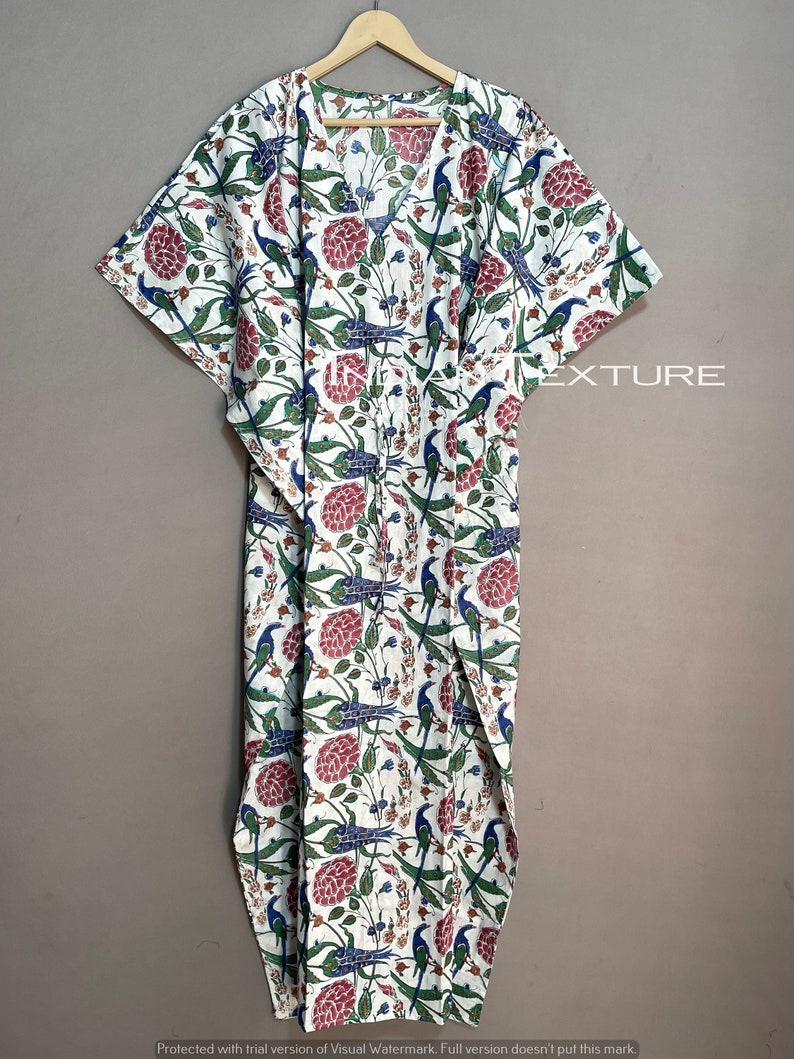 May include: White caftan with a floral and bird pattern in red, blue, and green. The long, flowing garment features a V-neck and wide sleeves. The fabric is printed with a repeating design of stylized birds and flowers.