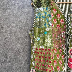 May include: A green quilted vest with a floral patchwork design. The vest has a V-neck and a tie closure at the waist.