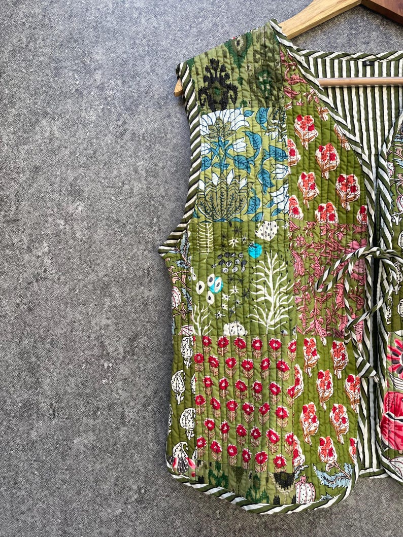May include: A green quilted vest with a floral patchwork design. The vest has a V-neck and a tie closure at the waist.