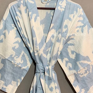K&ouml;nnte beinhalten: Eine hellblaue Baumwollrobe mit einem wei&szlig;en abstrakten Muster. Die Robe hat einen Bindeg&uuml;rtel und lange &Auml;rmel.
