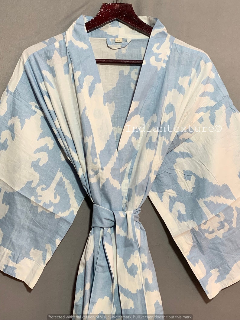 K&ouml;nnte beinhalten: Eine hellblaue Baumwollrobe mit einem wei&szlig;en abstrakten Muster. Die Robe hat einen Bindeg&uuml;rtel und lange &Auml;rmel.
