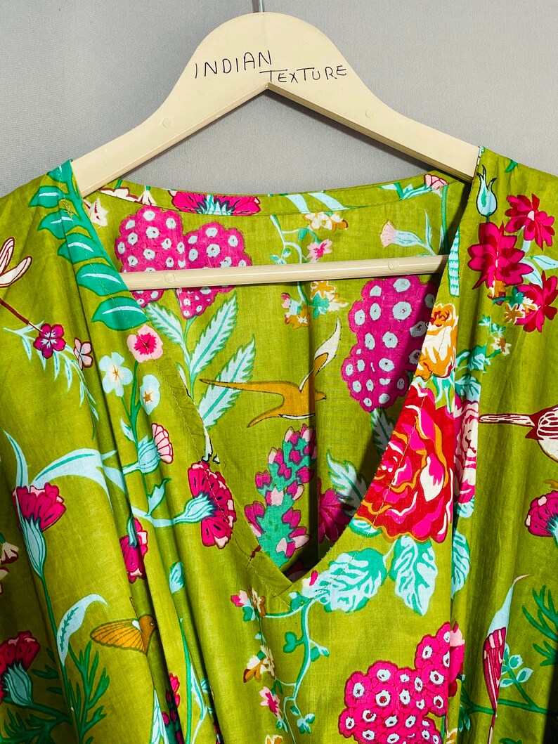 Peut inclure: Un tissu en coton vert avec un imprim&eacute; floral compos&eacute; de fleurs roses, rouges et blanches, de feuilles vertes et d'oiseaux. Le tissu est sur un cintre en bois avec le texte "INDIAN TEXTURE" &eacute;crit dessus.
