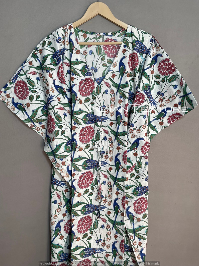May include: White caftan with a V-neck and short sleeves, adorned with a floral and bird pattern in red, blue, and green. The fabric is lightweight, and the design includes a drawstring waist.