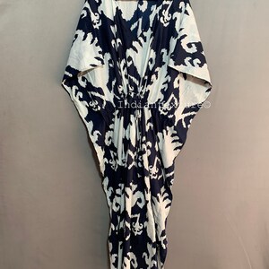 May include: A white and navy blue kaftan with a geometric pattern. The kaftan has a V-neck and a drawstring waist.