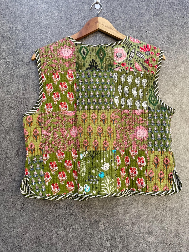 May include: A sleeveless quilted waistcoat with a patchwork design. The waistcoat is made of green fabric with floral patterns in pink, white, and blue. The waistcoat has a white and black striped trim around the edges.