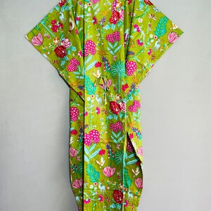 Peut inclure: Une kaftan en coton vert avec un imprim&eacute; floral compos&eacute; de fleurs roses, bleues et blanches, d'oiseaux et de cerfs. La kaftan a une ceinture &agrave; la taille et une silhouette longue et fluide.