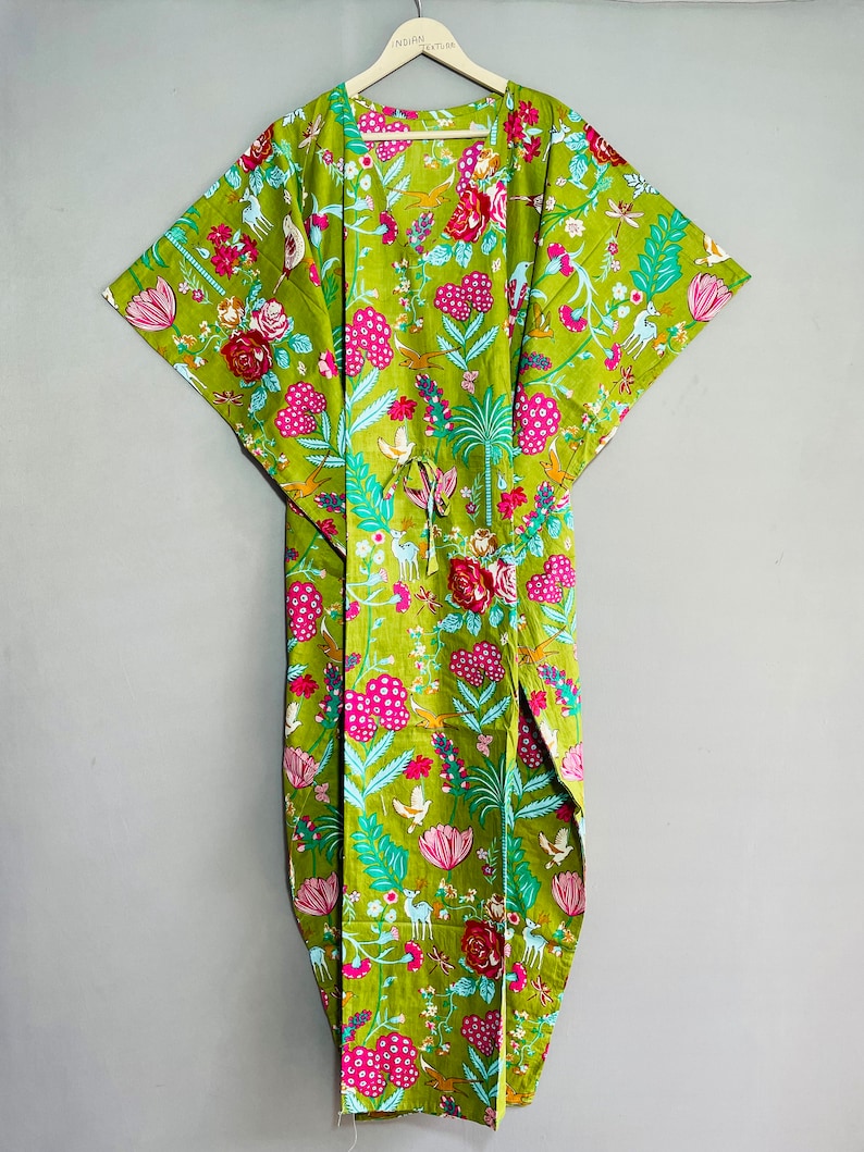 Peut inclure: Une kaftan en coton vert avec un imprim&eacute; floral compos&eacute; de fleurs roses, bleues et blanches, d'oiseaux et de cerfs. La kaftan a une ceinture &agrave; la taille et une silhouette longue et fluide.
