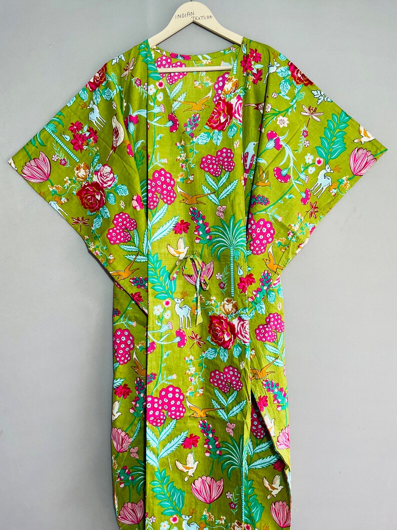 Peut inclure: Un kimono en coton vert avec un imprim&eacute; floral compos&eacute; de fleurs roses, rouges, bleues et blanches, d'oiseaux et de cerfs. Le kimono a un col en V et des manches larges. Le texte "INDIAN TEXTURE" est imprim&eacute; sur le cintre.
