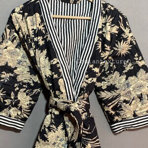 May include: A black quilted robe with a floral pattern in beige and blue. The robe has a striped white and black collar and cuffs. The robe is tied with a matching belt. The text "INDIAN TEXTURE" is visible on the hanger.