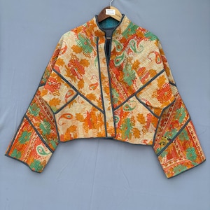 May include: A cropped jacket featuring a vibrant, multi-coloured floral and paisley pattern in shades of orange, yellow, and green. The garment is constructed with visible kantha-style stitching and is finished with dark grey piping along the seams.