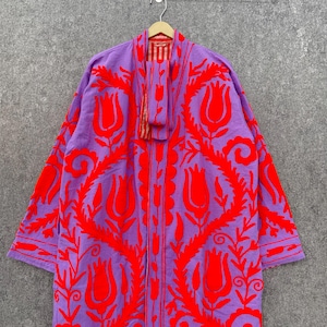 Puede incluir: Una larga t&uacute;nica morada con un estampado floral rojo. La t&uacute;nica tiene manga larga y cuello chal. La t&uacute;nica est&aacute; hecha de una tela suave y ligera.