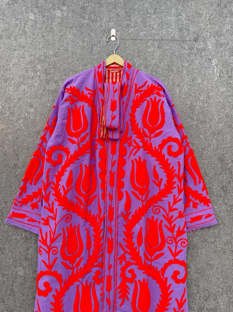 Puede incluir: Una larga t&uacute;nica morada con un estampado floral rojo. La t&uacute;nica tiene manga larga y cuello chal. La t&uacute;nica est&aacute; hecha de una tela suave y ligera.