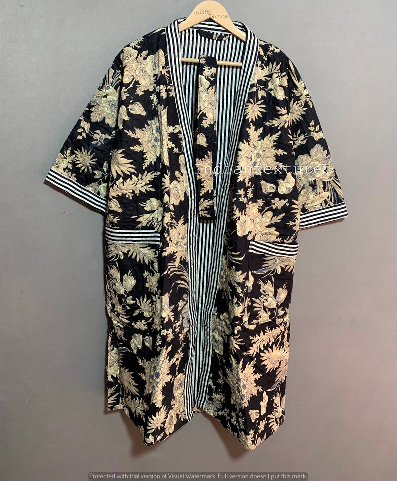 May include: A black floral print robe with a striped center panel and trim. The robe features a beige floral pattern on a black background. The sleeves and pockets are trimmed with white and black stripes. The robe is hanging on a wooden hanger.