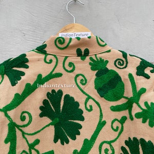 Op de afbeelding: Een beige katoenen jas met groene geborduurde bloemenmotieven. De jas heeft een kraag en een knoopsluiting. De borduursels omvatten spiralen, bladeren en bloemen.